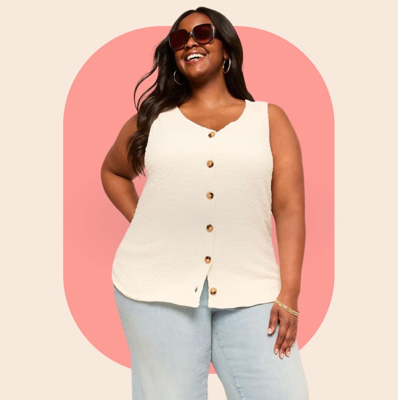A smiling woman in a cream-colored button-up tank top and light blue jeans stands against a soft pink and beige oval background.