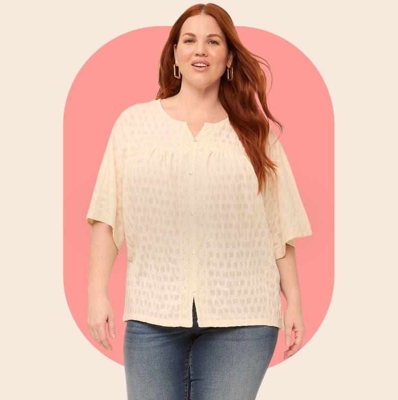 A woman with red hair smiles while wearing a cream-colored textured blouse and blue jeans, set against a soft pink oval on a beige background.