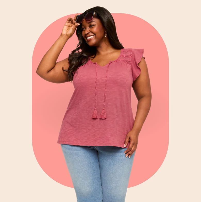 A smiling woman in a pink top and jeans poses against a peach-colored oval background.