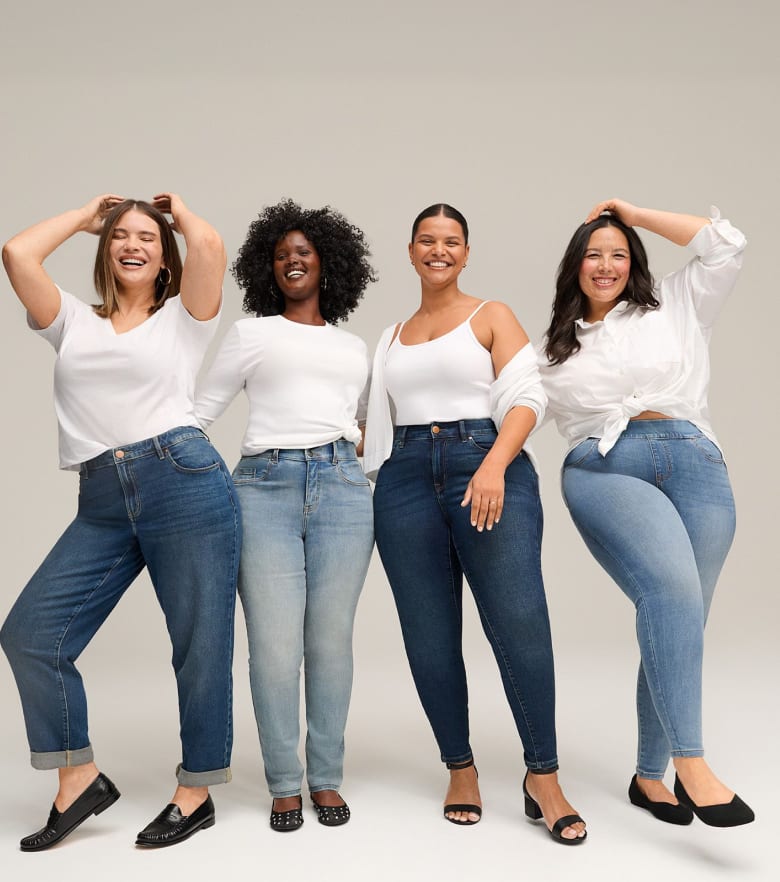 Four women in jeans and white tops pose against a plain, light background.