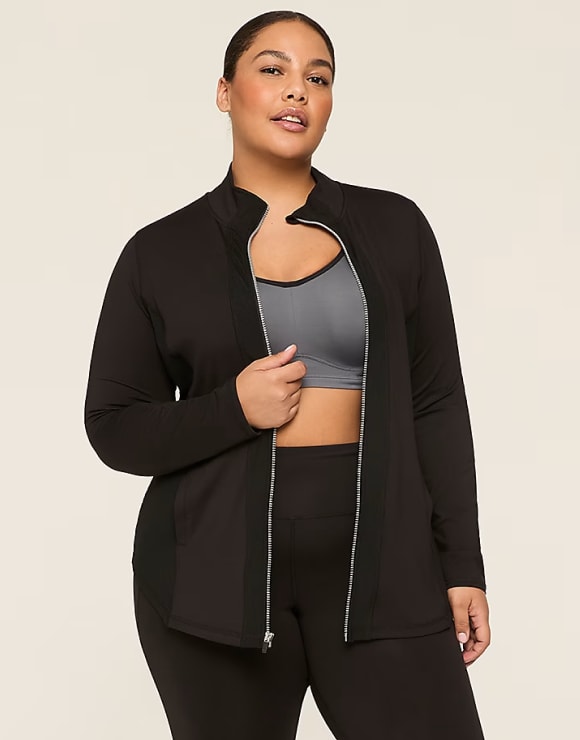 A plus-size woman in a black zip-up jacket and gray sports bra stands against a plain, light-colored background.