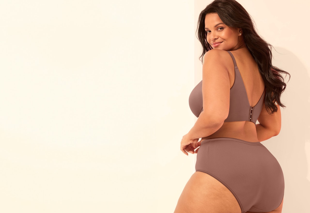 A woman in a mauve bra and high-waisted underwear poses against a plain, light-colored background.