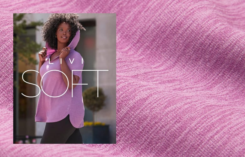 A woman in a pink hooded top stands in front of a blurred urban background, with a textured pink fabric filling the foreground.