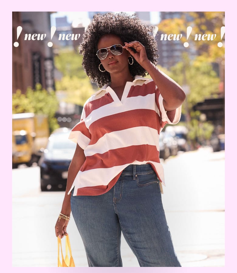 A woman in a striped shirt and jeans stands on a city street with blurred traffic in the background.