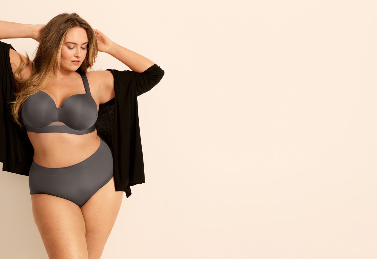 A woman in gray lingerie and a black cardigan poses against a plain, light-colored background.
