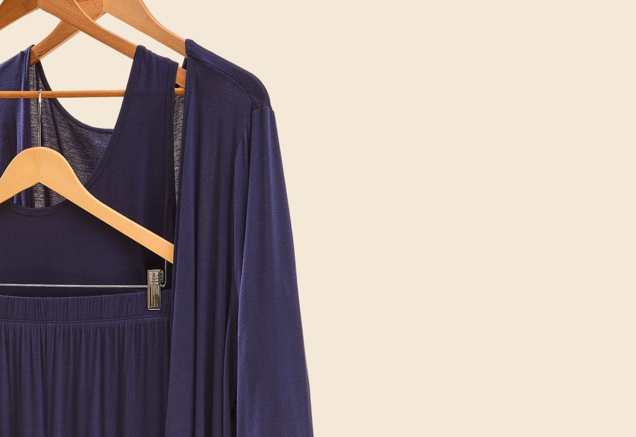 Two navy blue outfits hang on wooden hangers against a plain, light beige background.