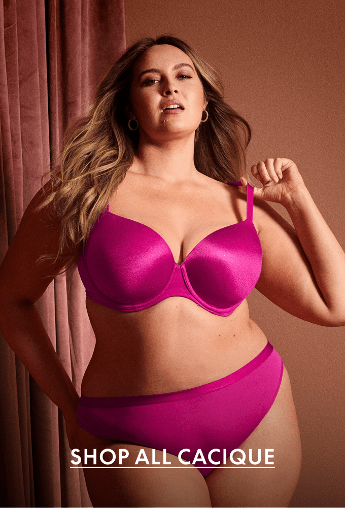 A woman in a pink bra and underwear stands in front of a draped pink curtain.