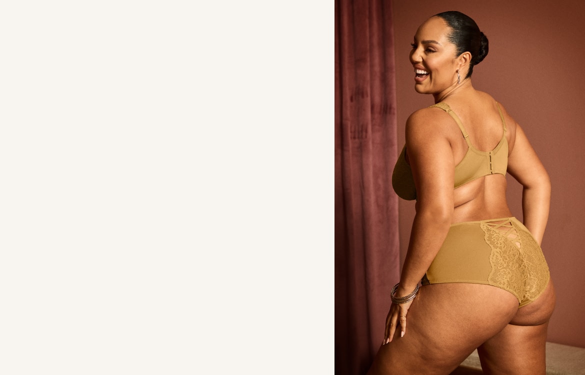 A woman in tan lingerie smiles over her shoulder against a muted pink backdrop.