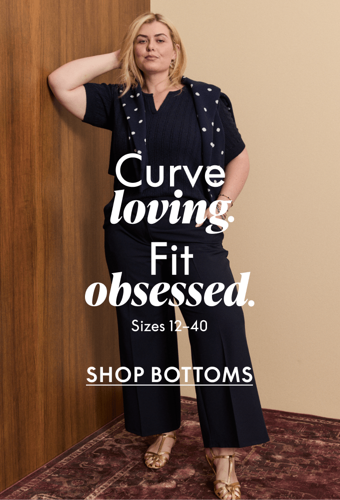 A plus-size woman in navy blue attire stands against a warm-toned wall with a patterned rug in the foreground