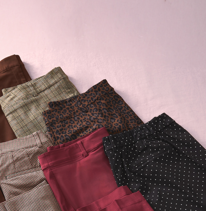 Several pairs of patterned pants are neatly folded in the foreground against a soft pink background.
