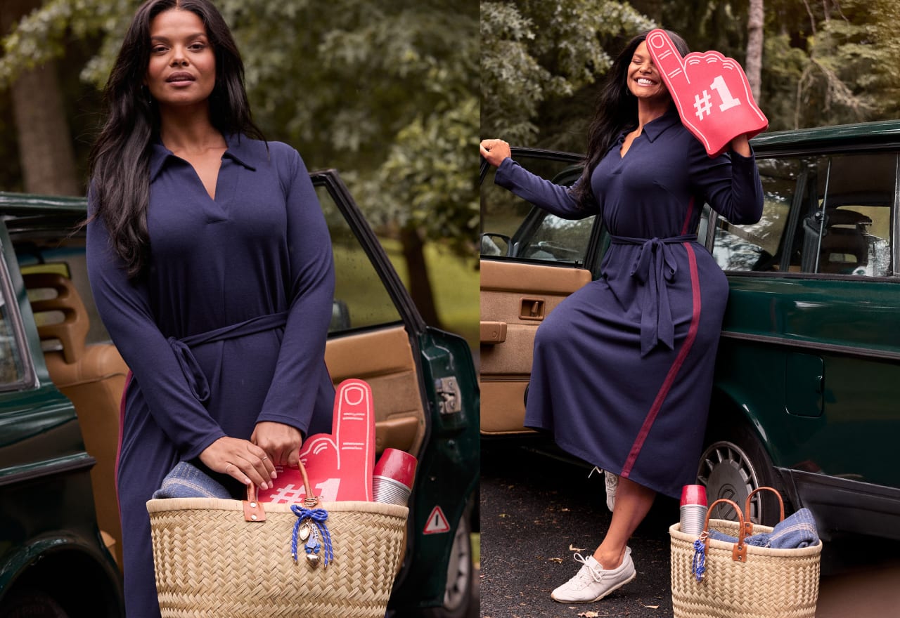 A woman in a navy dress stands by a car, holding a foam finger and a basket of fan gear, with trees in the background.