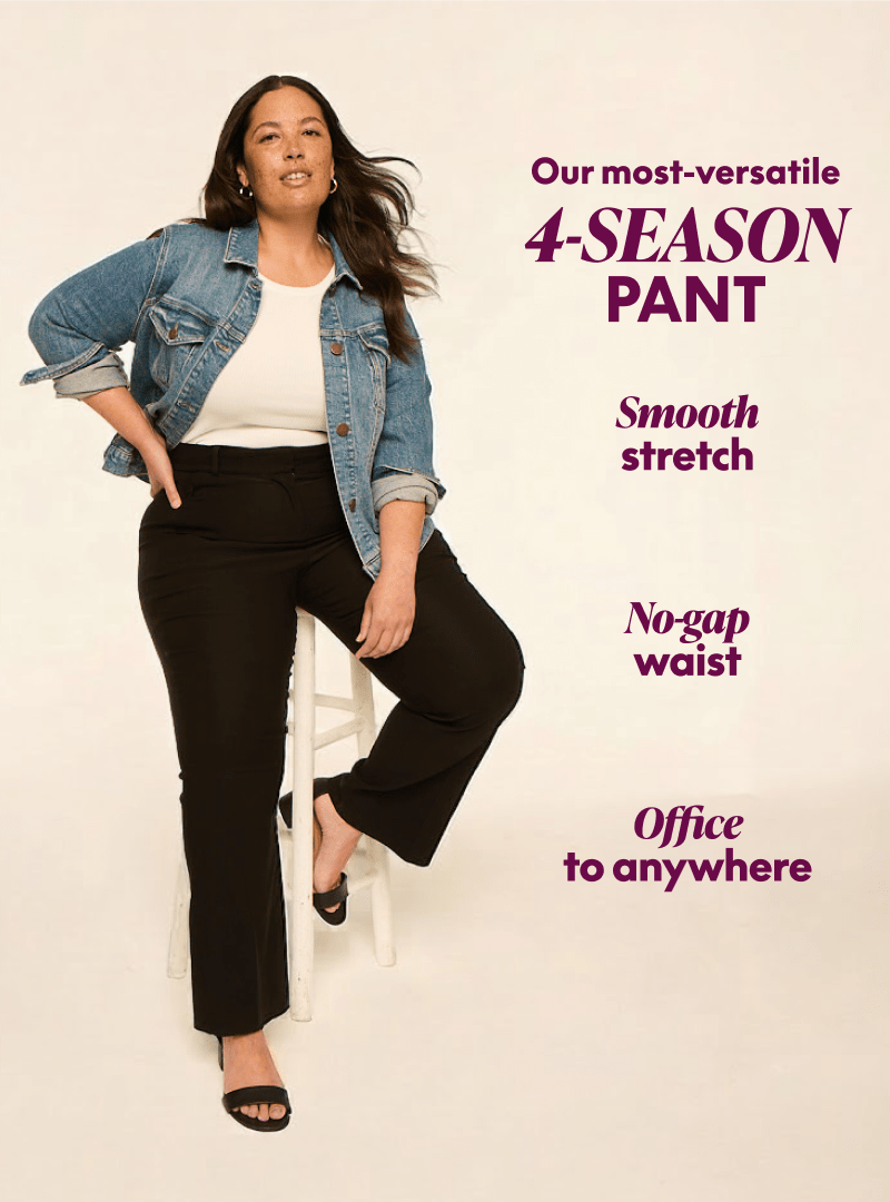 A smiling woman in a cream top and navy pants sits on a wooden chair against a plain, light background.