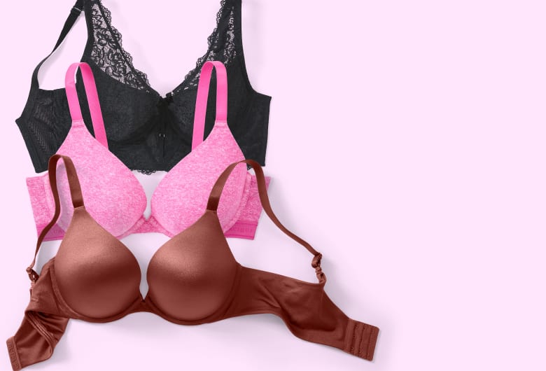 Three bras, a brown, a pink, and a black one, are neatly stacked on a light pink background.