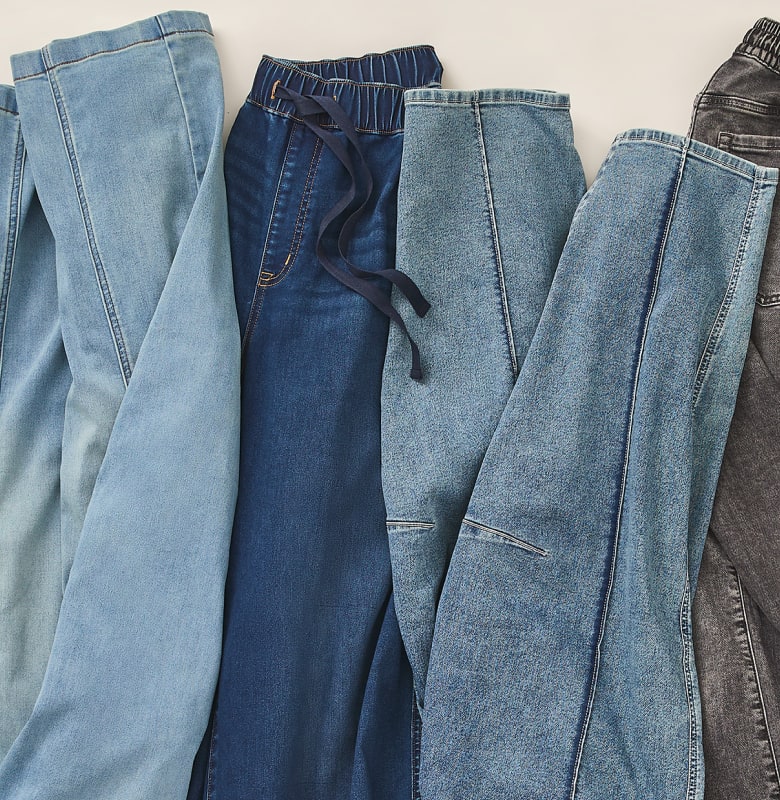 Several pairs of denim pants in various shades of blue and gray are laid out on a white background.
