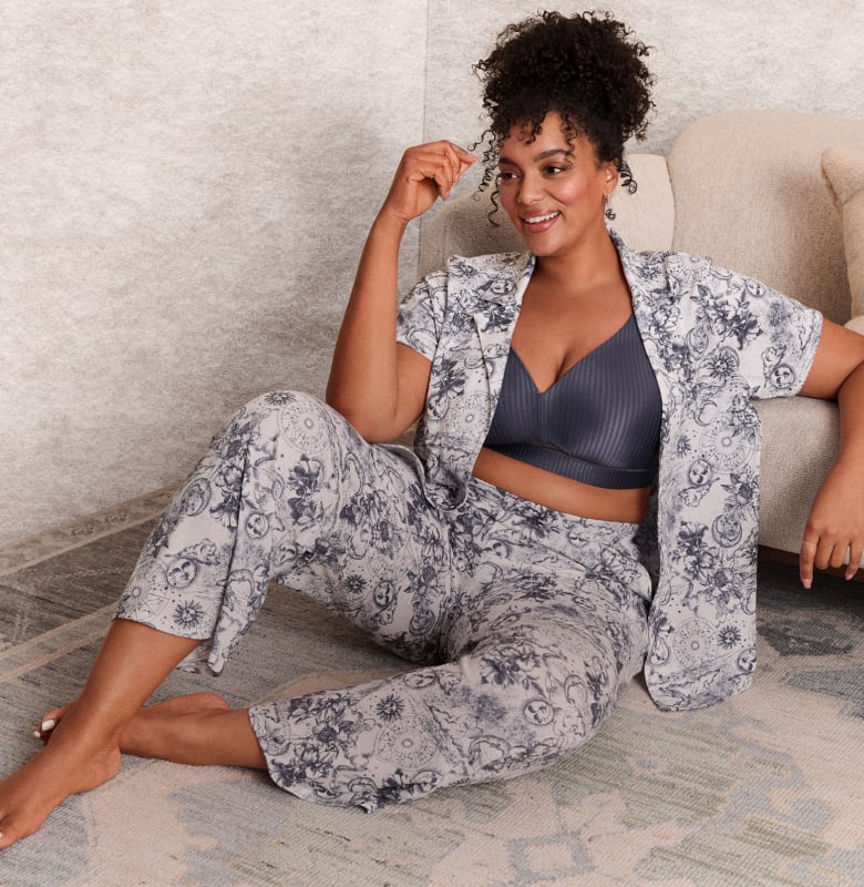 Three women in loungewear are shown against a neutral background, with one woman sitting on the floor and the other two standing.