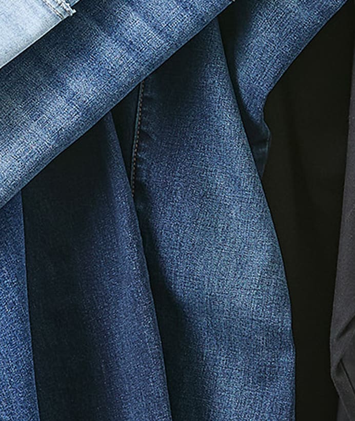 Several folded pairs of blue denim jeans are stacked against a dark background.