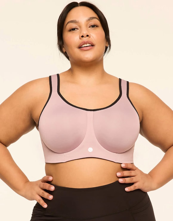 A woman with her hands on her hips wears a mauve sports bra with black trim against a plain, light background.
