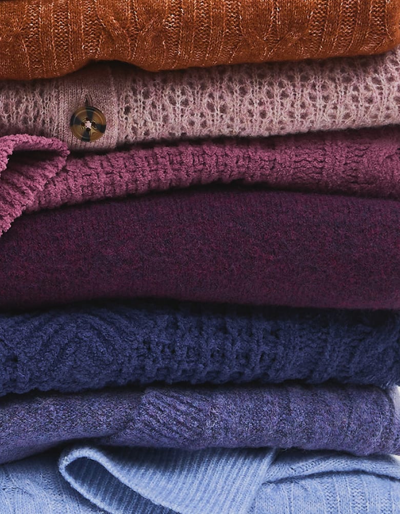 A stack of colorful knitted sweaters in shades of orange, pink, purple, and blue fills the entire frame.