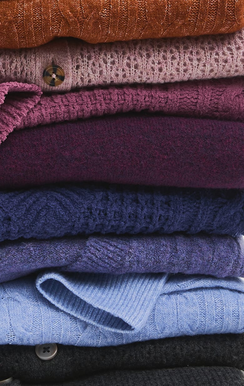 A stack of colorful knitted sweaters in shades of orange, pink, purple, and blue fills the entire frame.