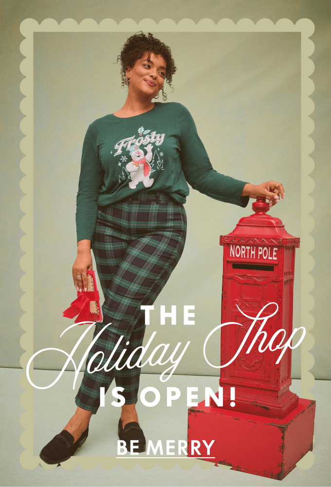 A woman wearing a green Frosty the Snowman shirt and plaid pants leans against a red North Pole mailbox against a plain light-blue background.