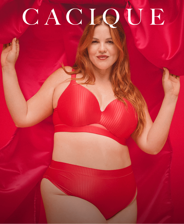 A woman with red hair wearing a red lingerie set poses against a backdrop of draped red satin fabric.