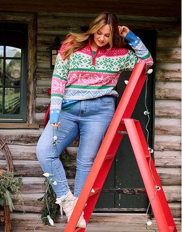 A woman wearing a grey and white patterned two-piece set stands in front of a white wooden shed.