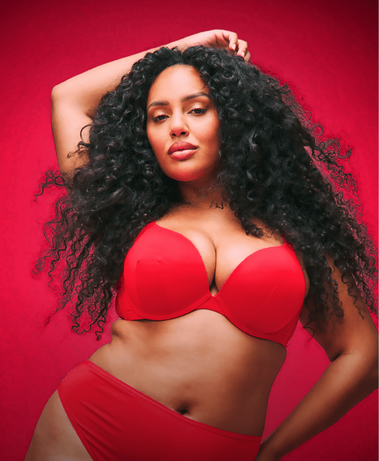A smiling woman wearing a black sparkling lingerie set poses against a solid bright red background.