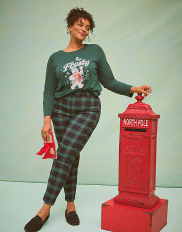 A woman wearing a grey and white patterned two-piece set stands in front of a white wooden shed.
