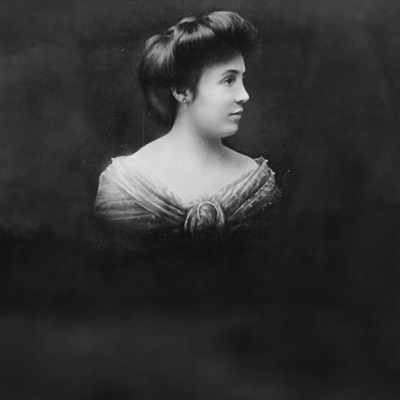 A woman with her hair styled up poses in a formal dress against a dark, blurred background.