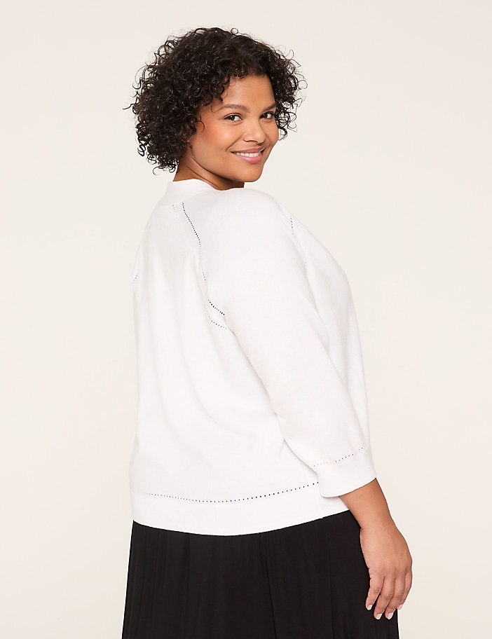 A smiling young woman with curly dark hair wearing a white sweater stands against a plain light-colored background.