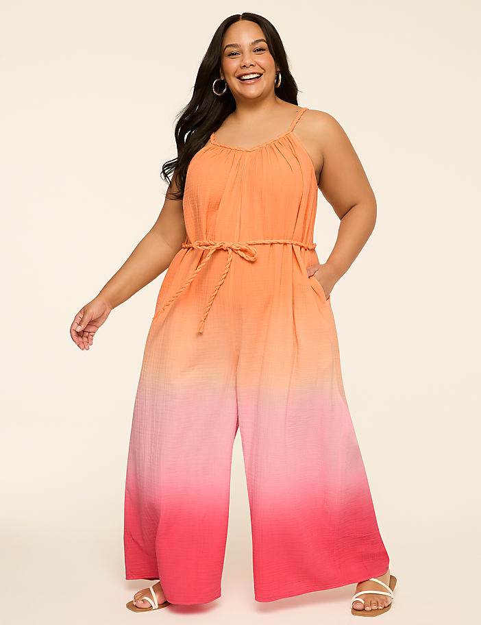 A smiling woman in a colorful ombre jumpsuit stands against a plain, light-colored background.
