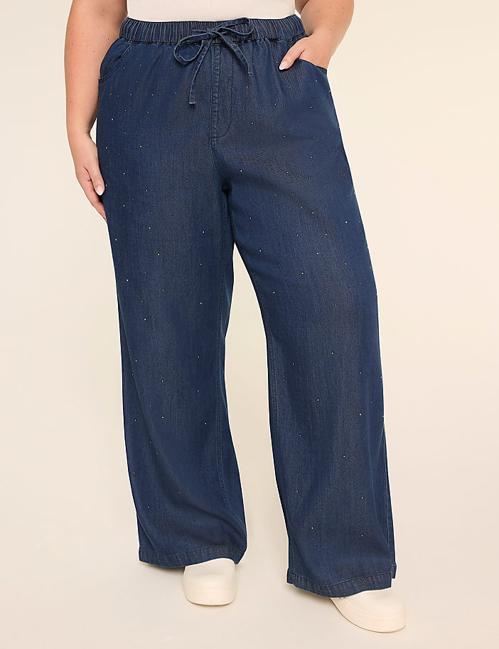 Navy blue denim pants with white polka dots, worn by a person's lower body standing on a light-colored background.