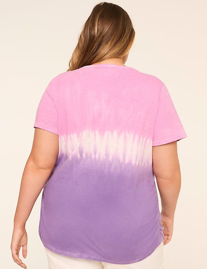 The image shows a woman's back, with her long brown hair visible. She is wearing a pink and purple tie-dye t-shirt against a plain light-colored background.