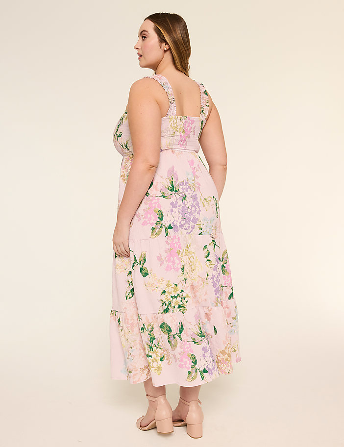 A woman wearing a floral print dress stands in a neutral-colored setting, her back facing the camera.