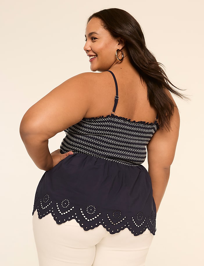 A smiling woman with long dark hair wearing a patterned top and a black skirt with a scalloped hem stands against a plain background.
