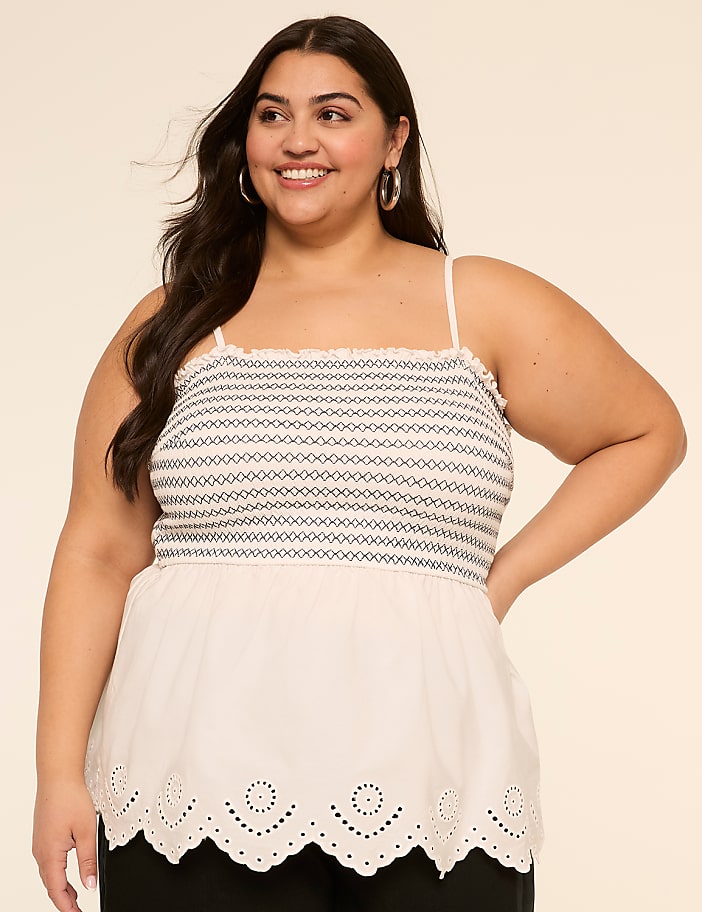 A smiling young woman wearing a white sleeveless top with a patterned bodice and a scalloped hem stands against a plain beige background.