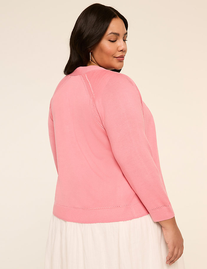 A woman with dark hair wearing a pink sweater stands against a plain beige background.