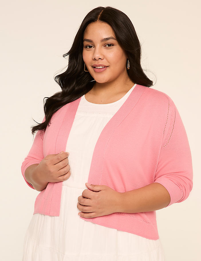 A young woman with long dark hair is wearing a pink cardigan and a white top, standing against a plain background.