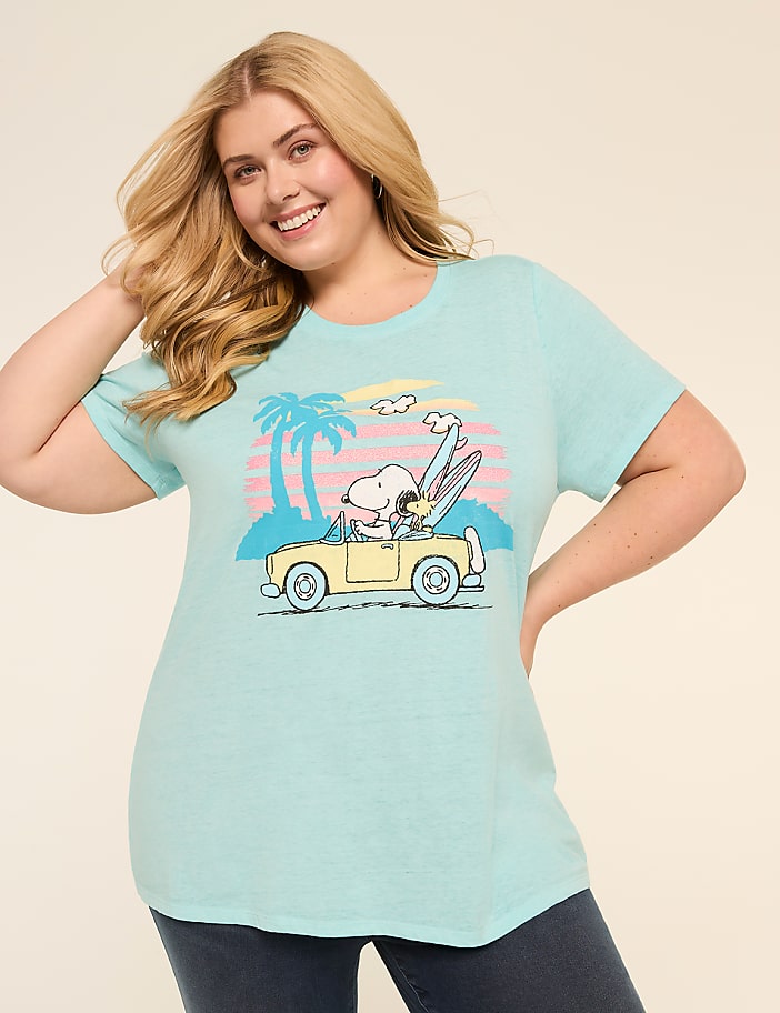 A smiling young woman with long blonde hair wearing a turquoise t-shirt featuring a cartoon image of Snoopy driving a car on a beach with palm trees in the background.
