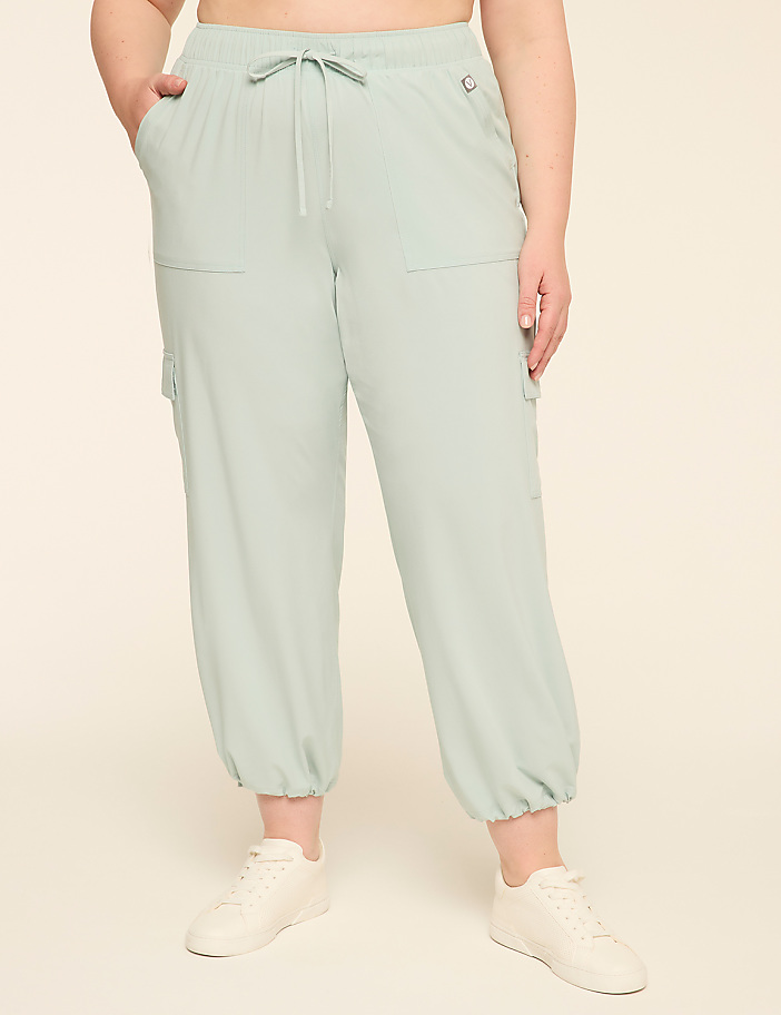 A person wearing light green cargo pants and white sneakers stands against a plain, light beige background.