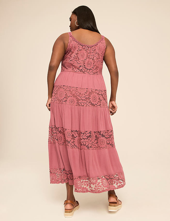 A woman in a mauve lace-trimmed maxi dress stands against a plain, light-colored background.