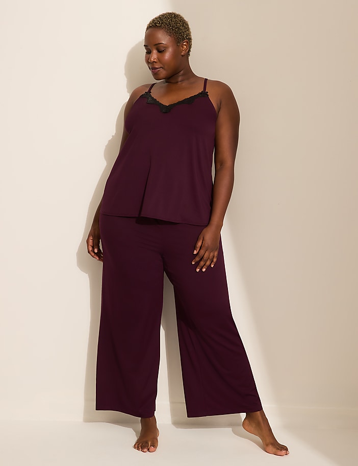 A woman in burgundy pajamas stands against a plain, light-colored wall.