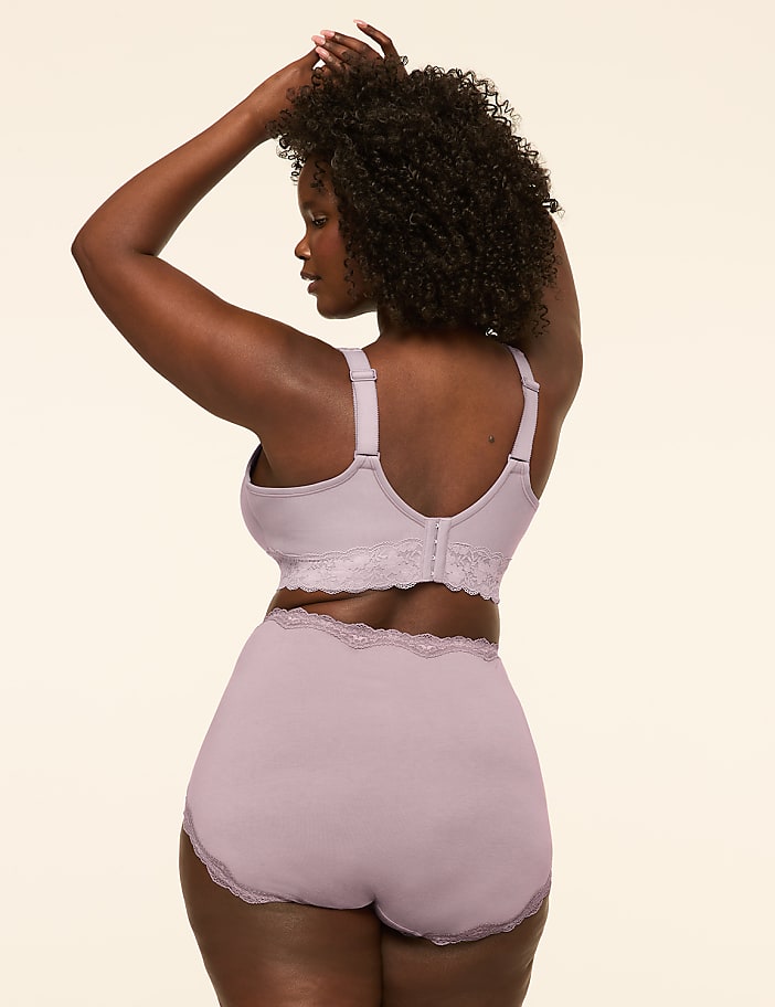 A woman in a lilac bra and high-waisted briefs with lace trim stands against a plain, light-colored background.