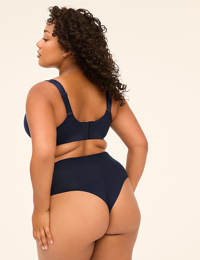 A woman in navy blue lingerie stands with her back to the viewer against a plain, light-colored background.