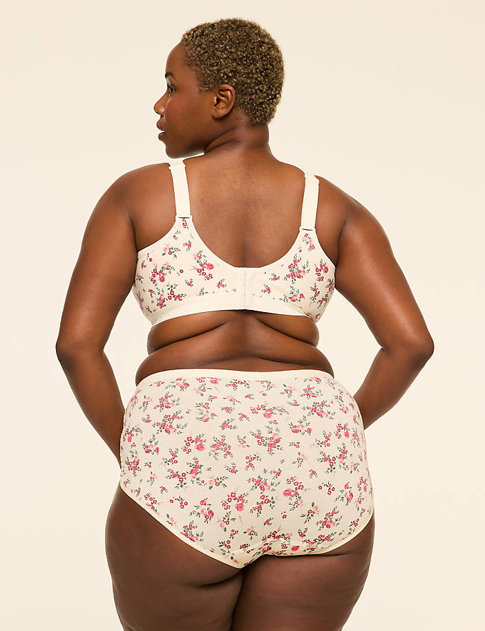 A woman in a floral bra and matching underwear stands against a plain, light-colored background.
