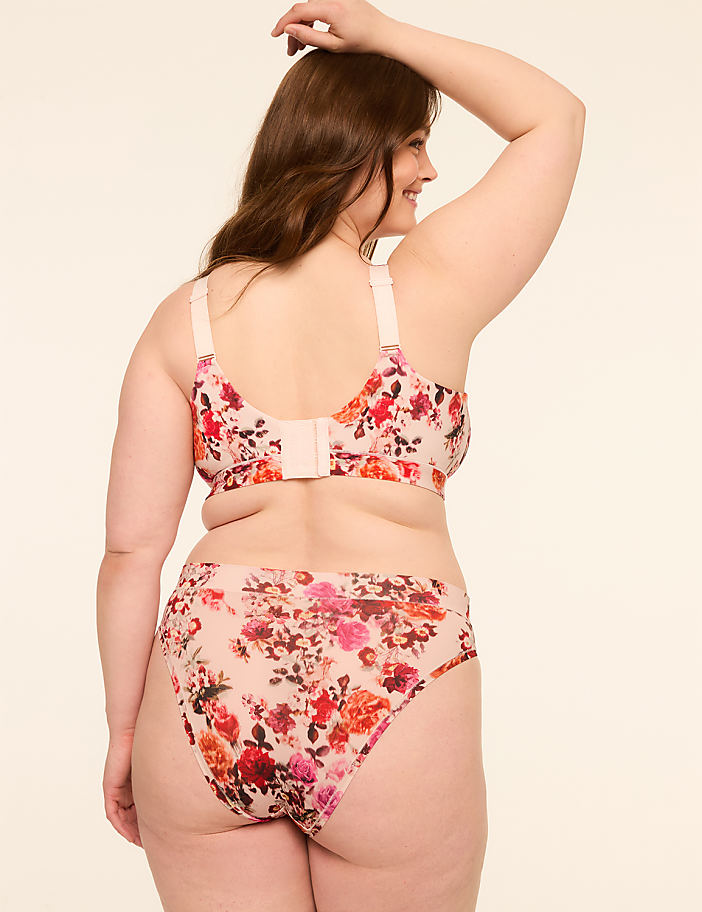 A woman in a floral bra and underwear stands against a plain, light-colored background.