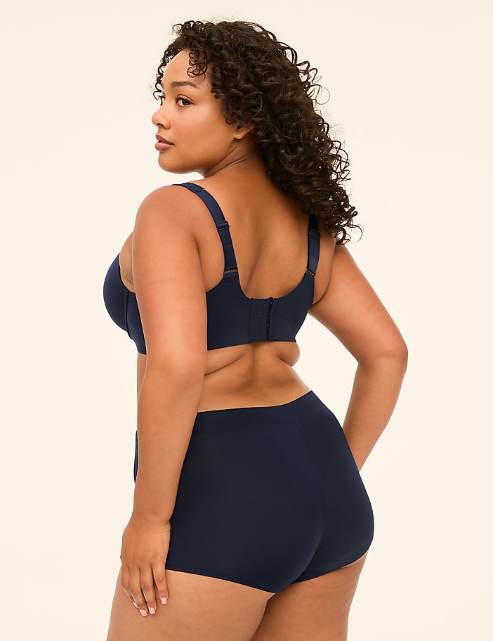 A woman in navy blue lingerie stands against a plain, light-colored background.