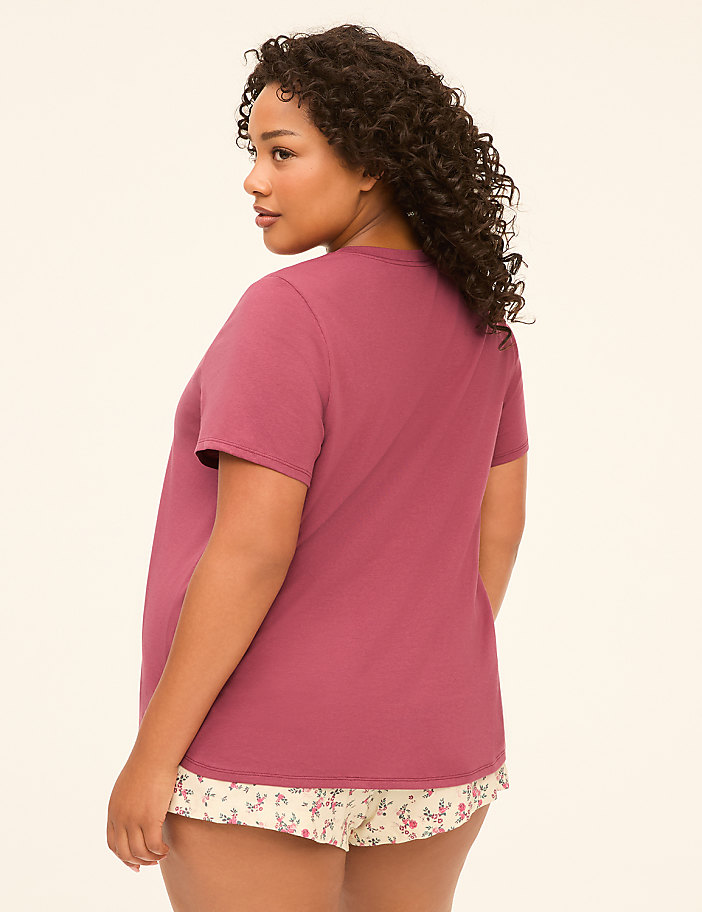 A woman in a mauve t-shirt and floral shorts stands against a plain, light-colored background.
