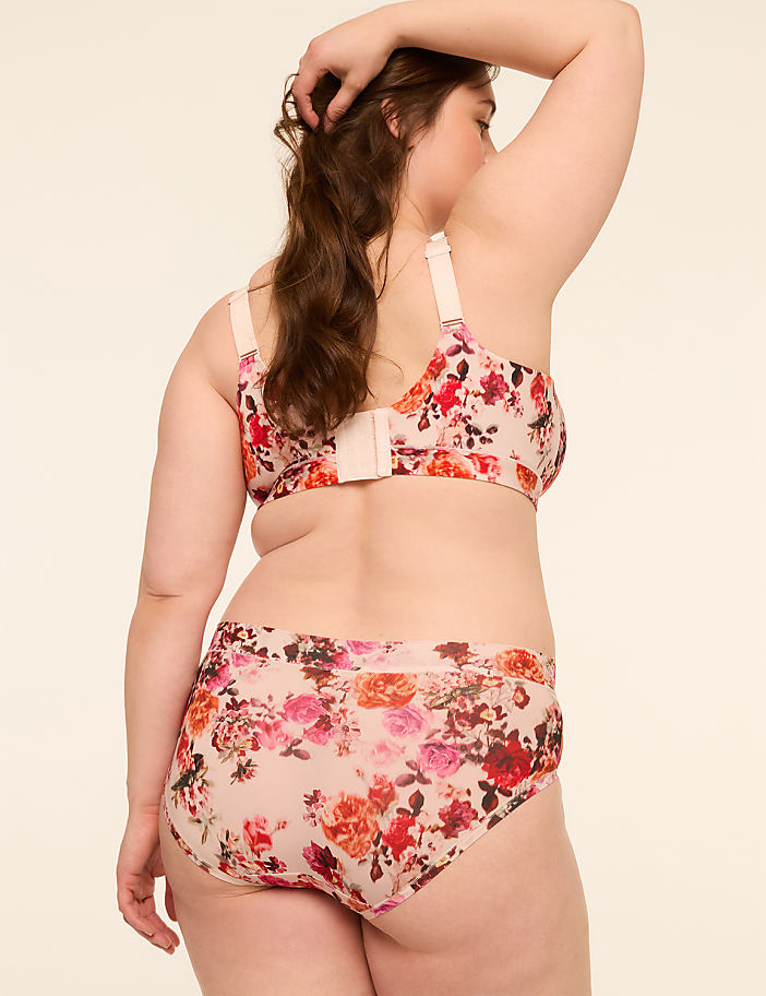 A woman in a floral bra and underwear stands against a plain, light-colored background.