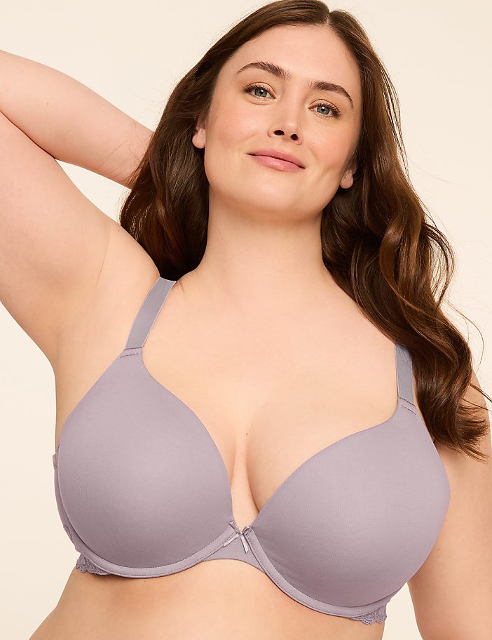 A woman with brown hair and a light complexion smiles as she poses in a light purple bra against a plain, light-colored background.